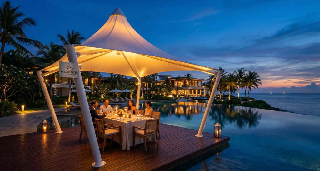 Custom conical tensile fabric gazebo by Peaknox illuminating a luxury resort outdoor dining area at twilight.
